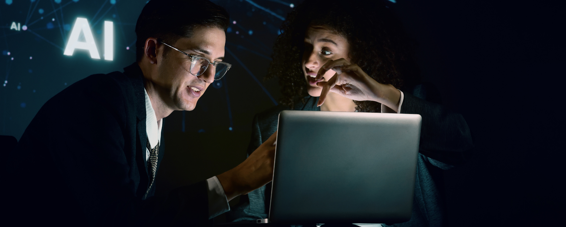 Dwie osoby wspólnie analizują laptop w ciemnym pomieszczeniu oświetlonym ekranem, z turkusową grafiką sieci AI w tle – wizualna metafora wspólnych decyzji architektonicznych Drupal multisite vs wielojęzyczność.