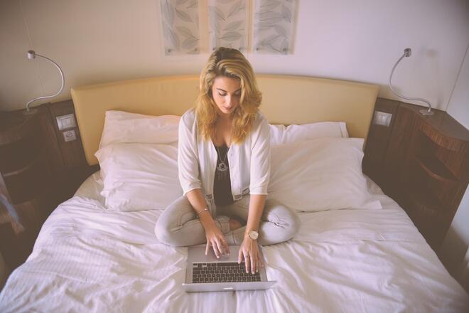 A woman sitting on the bed with a laptop, browsing Drupal websites
